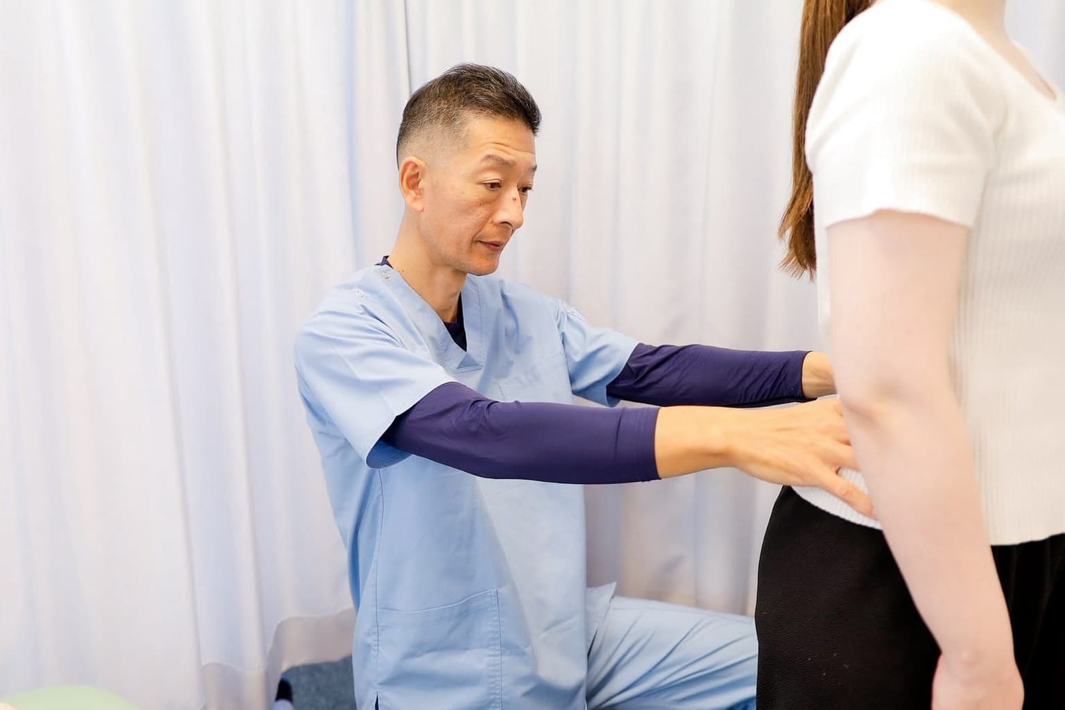 立った姿勢の患者さんの腰に手を当て、腰の状態を確認する清水接骨院の院長