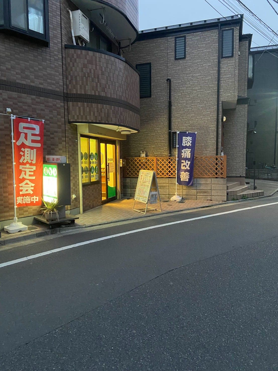 夕方の清水接骨院の外観。入口の明かりと、のぼり旗が立っている