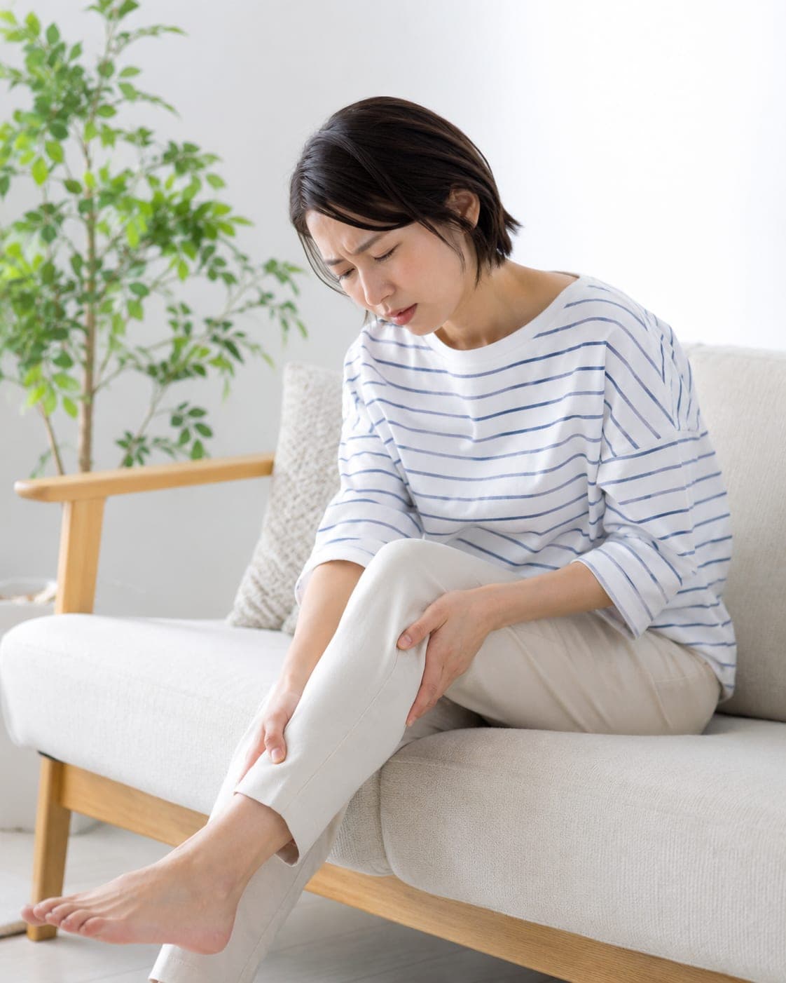 ソファに座ってふくらはぎを押さえる女性(イメージ)