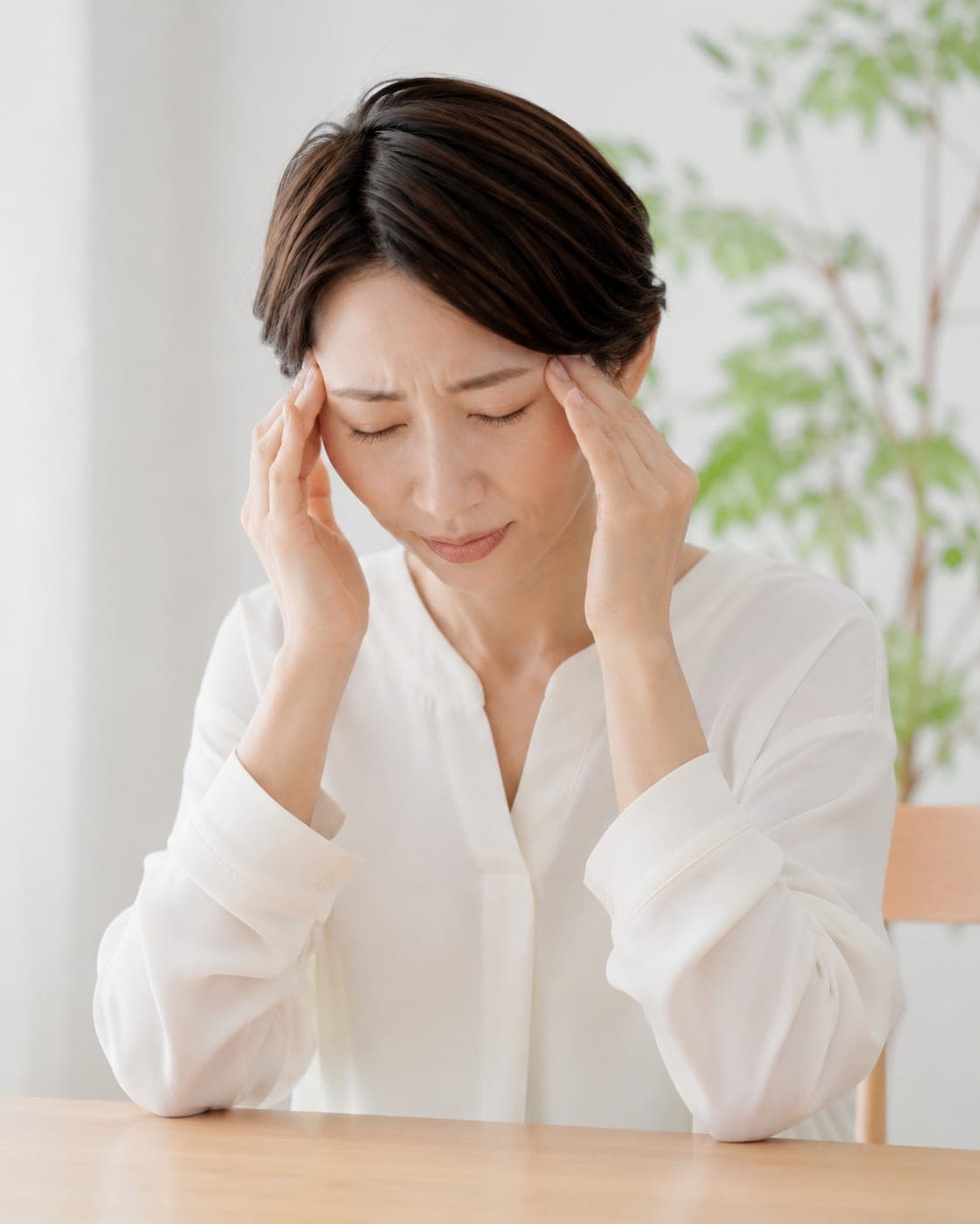 こめかみを押さえる女性(頭痛のイメージ)