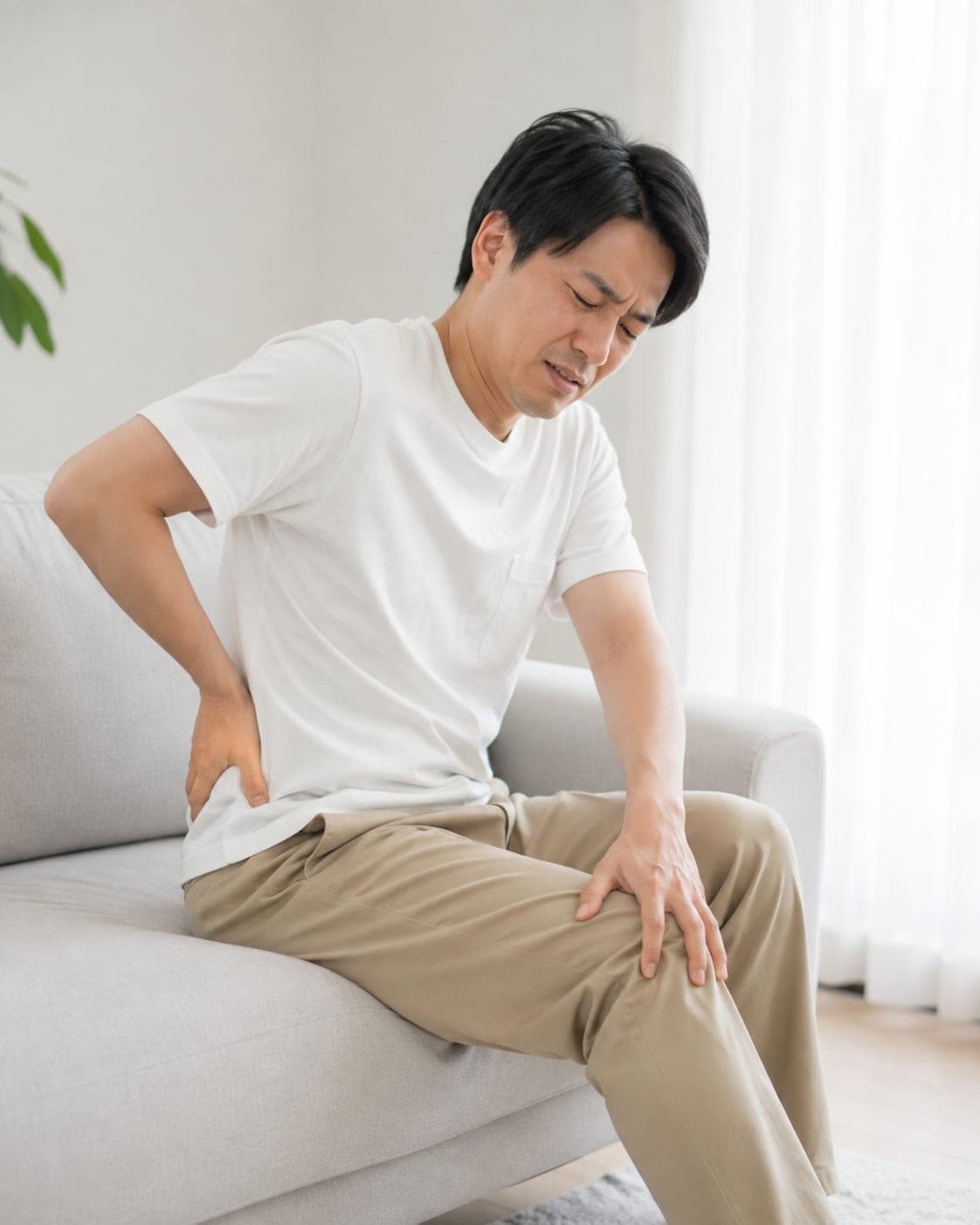 ソファで股関節の付け根から太ももを押さえる男性(イメージ)