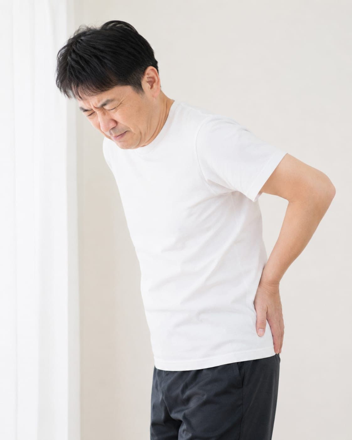 立ったまま腰から股関節を押さえる男性(イメージ)