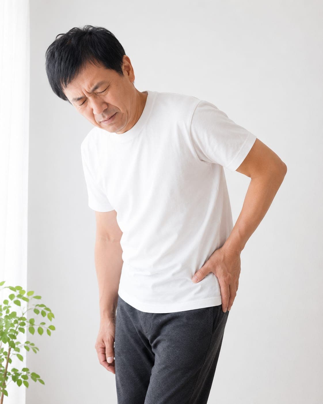 立ったまま腰から股関節を押さえる男性(イメージ)