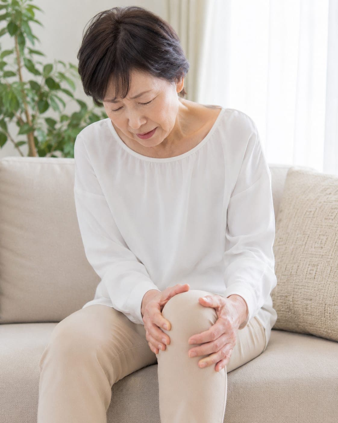 ソファで膝を押さえる年配の女性(イメージ)