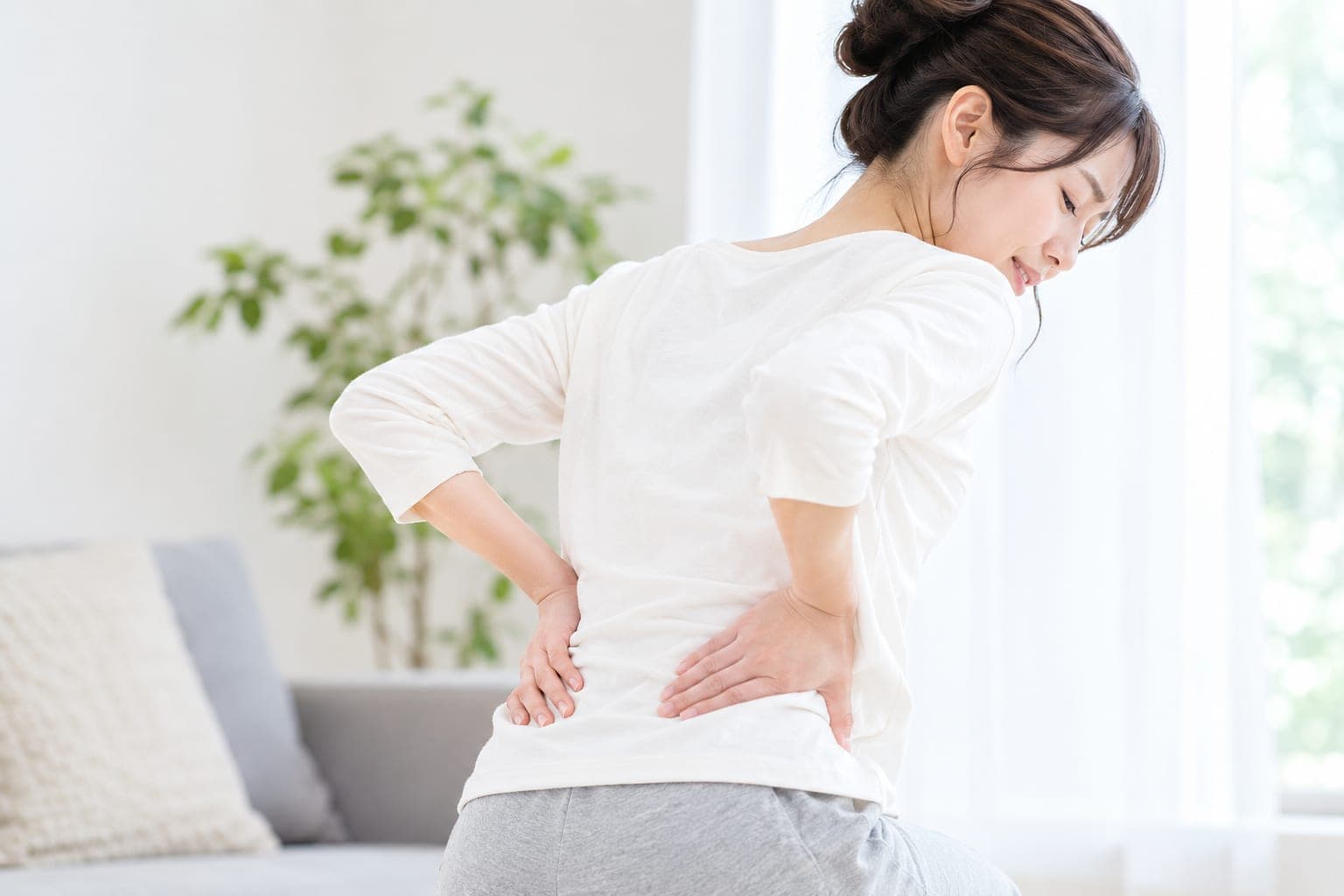 座って腰を押さえる女性の後ろ姿(イメージ)