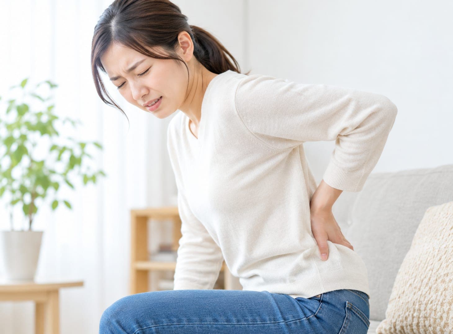 ソファに座って腰に手を当てる女性(イメージ)
