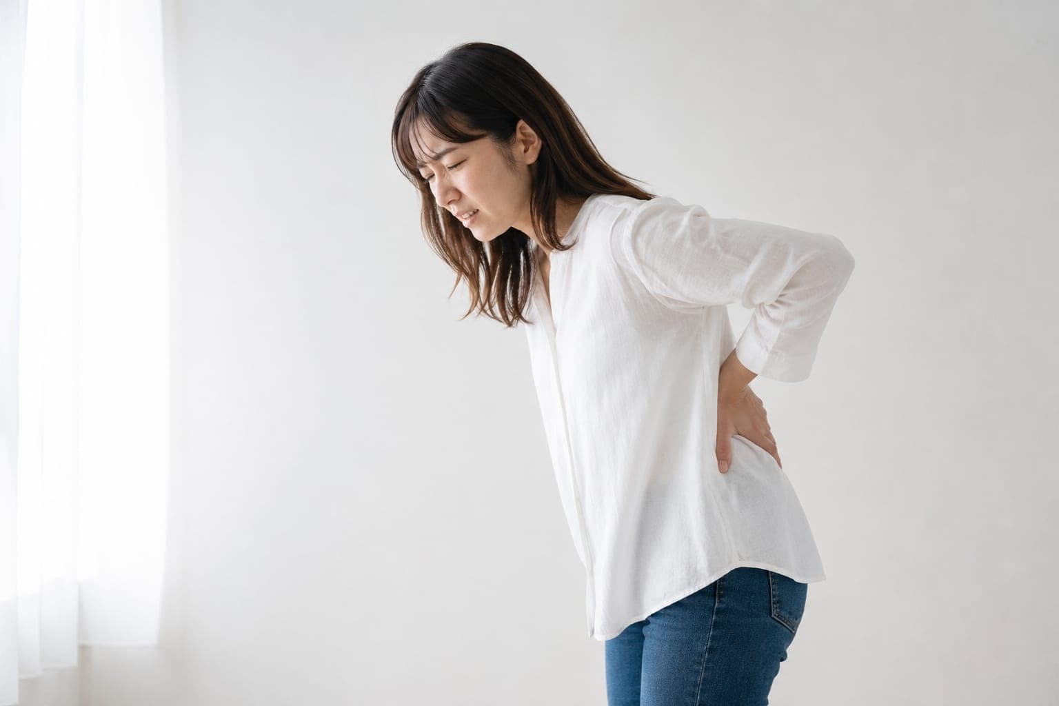 腰を押さえて立つ女性の横姿(イメージ)