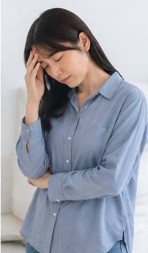 こめかみを押さえる女性(頭痛のイメージ)