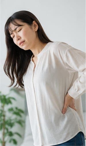 立ったまま腰を押さえる女性(イメージ)